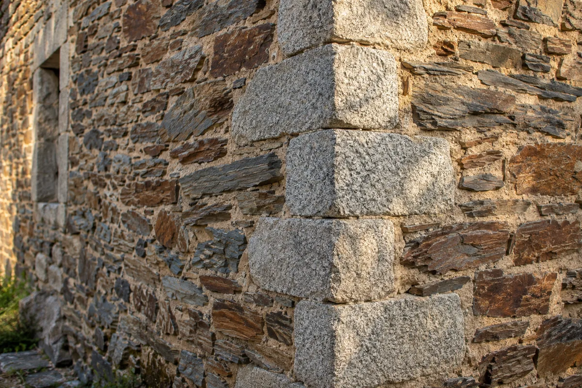 Mur ancien en moellons de schiste hourdé au mortier de chaux, chaîne d&rsquo;angle en granit, en lumière rasante