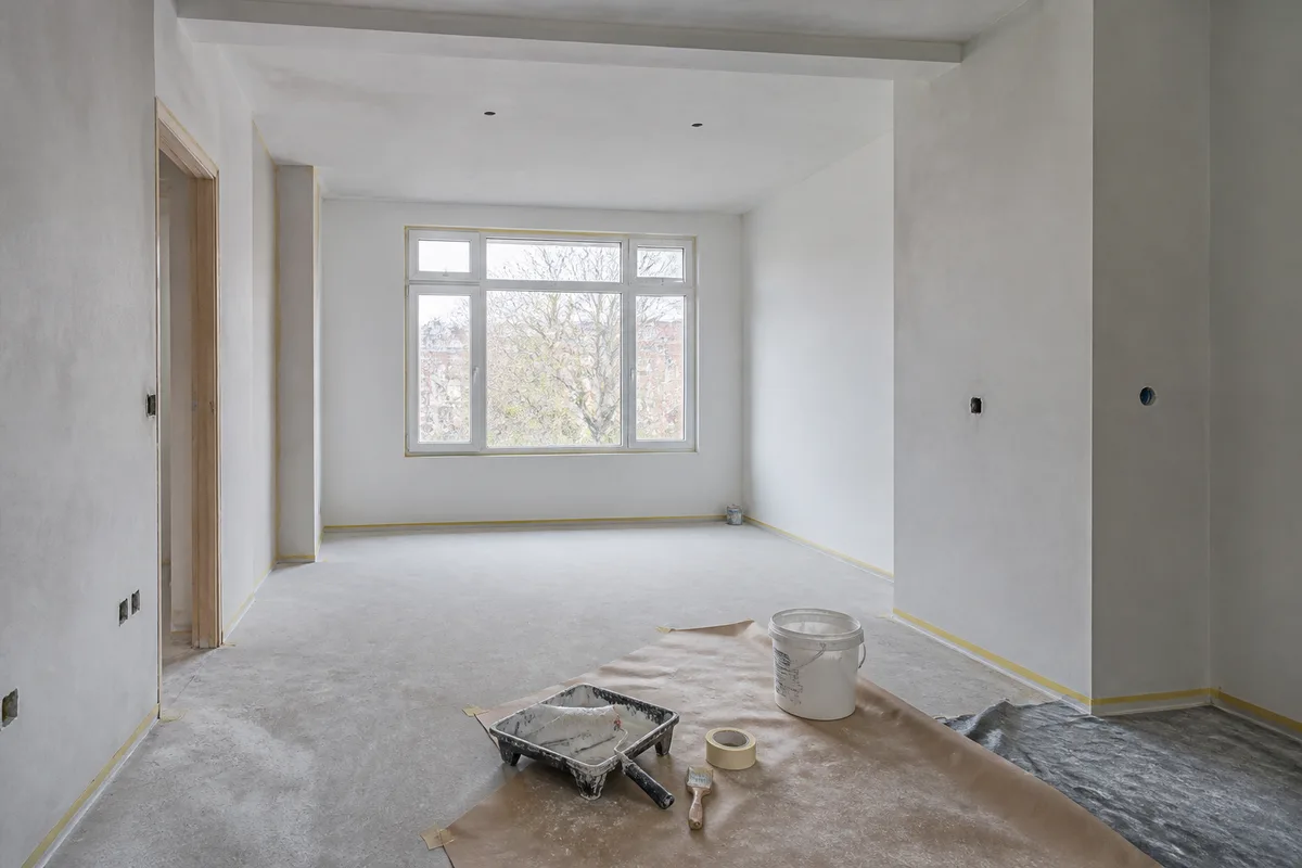 Pièce en fin de chantier avec murs enduits, ruban de masquage et outils de peintre au sol