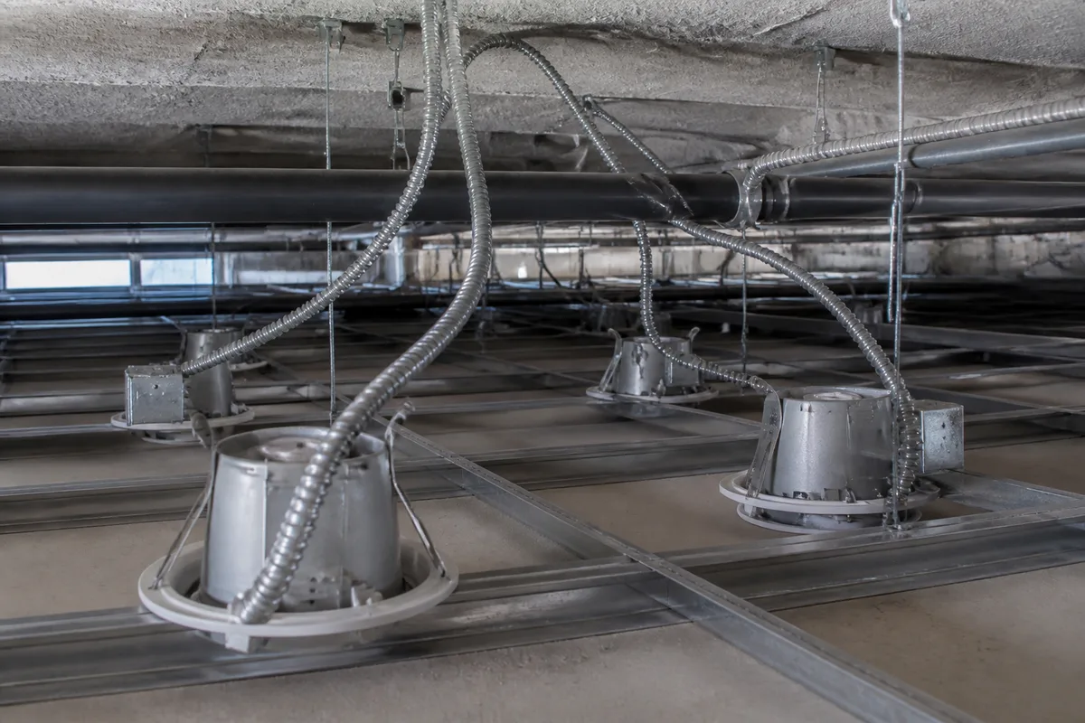 Gaines électriques et corps de spots encastrés positionnés dans le plénum d&rsquo;un plafond en travaux